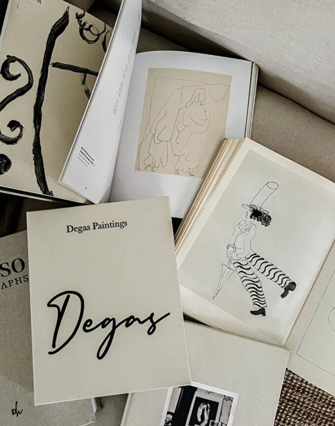Open art books featuring line drawings and sketches, with a closed book titled 'Degas Paintings' on a beige surface