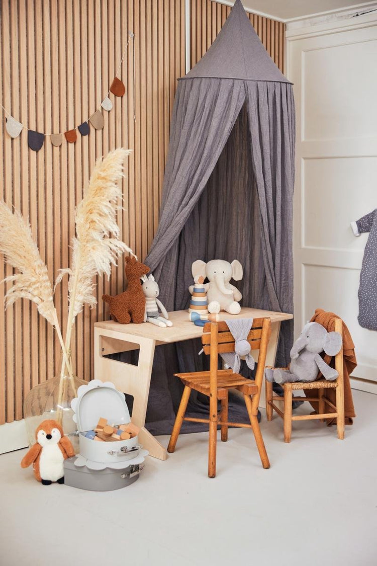 Cozy children's play area with wooden table, two chairs, stuffed animals, gray canopy, and pampas grass