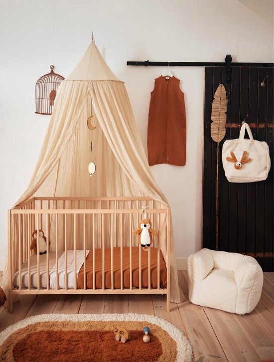Beige baby nursery with wooden crib, canopy, plush toys, cozy armchair, and brown rug