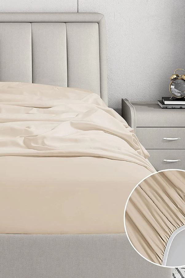 Beige fitted sheet on gray upholstered bed with matching nightstand and vintage alarm clock