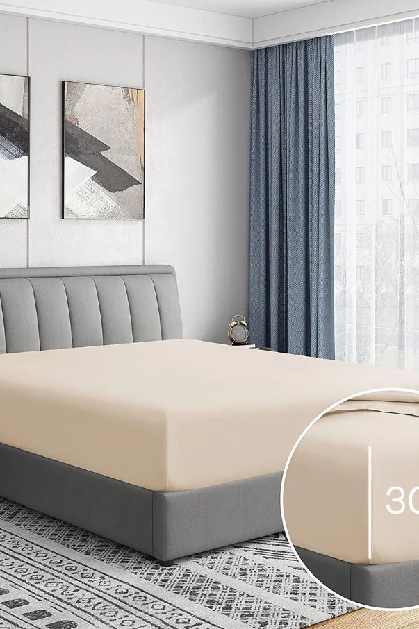 Modern bedroom with beige fitted sheet on gray upholstered bed, blue curtains, and abstract wall art