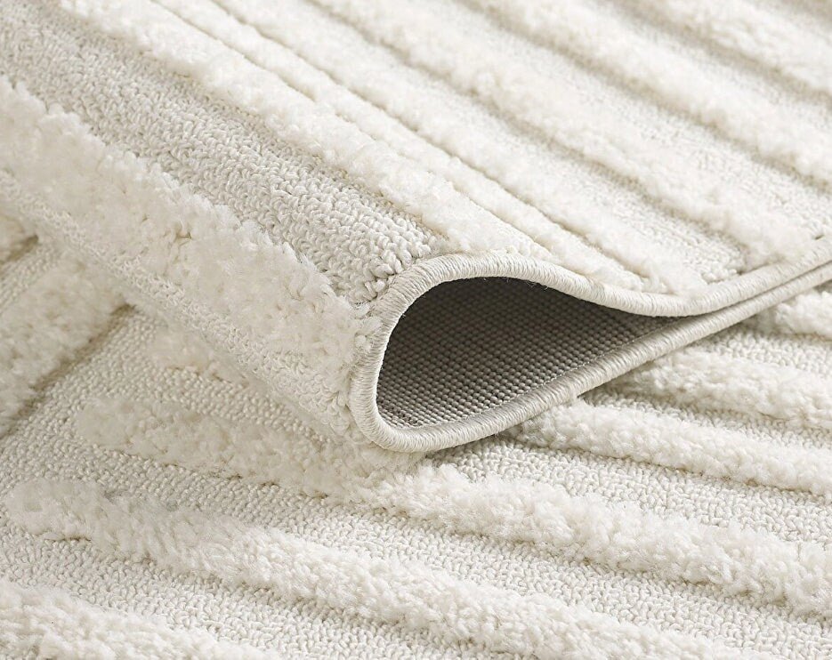Close-up of a folded cream textured area rug with raised striped pattern and stitched edges