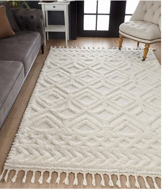 White textured geometric patterned area rug with fringe on hardwood floor between gray sofa and beige upholstered chair