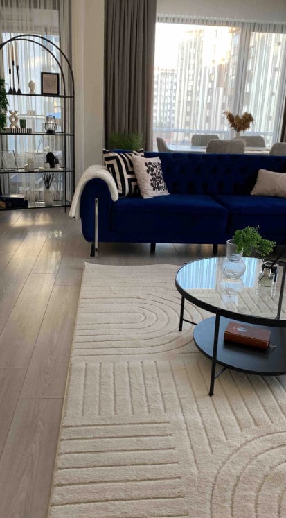Modern living room with navy blue velvet sofa, geometric patterned pillows, glass coffee table, and textured beige rug