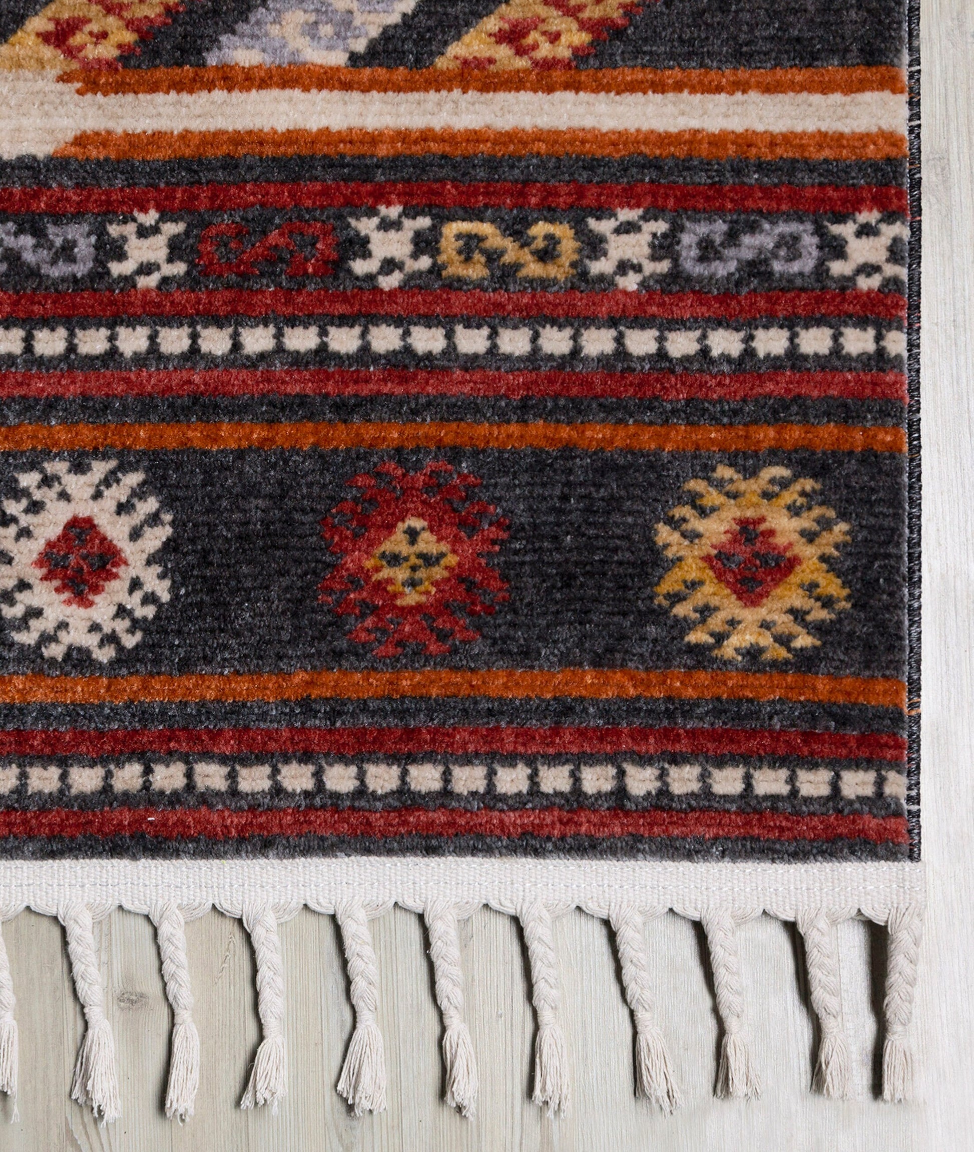 Close-up of a patterned area rug with geometric designs in red, orange, cream, and gray, featuring fringed edges