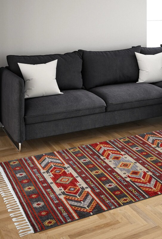 Dark gray sofa with white pillows on wooden floor next to a colorful geometric patterned area rug