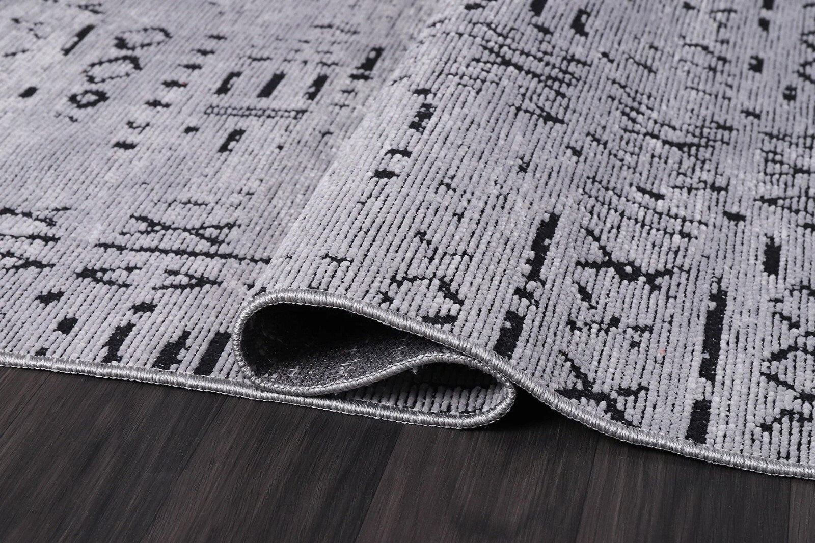 Close-up of folded modern gray and black patterned area rug on dark hardwood floor