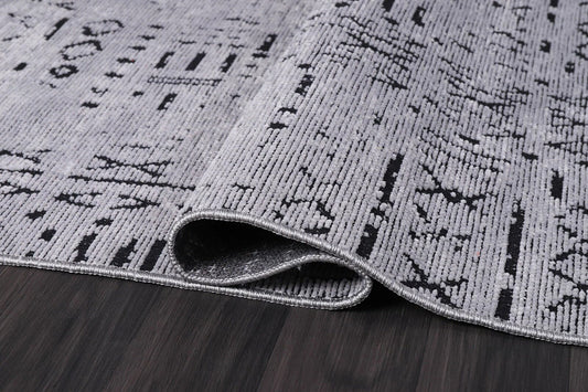 Close-up of folded modern gray and black patterned area rug on dark hardwood floor