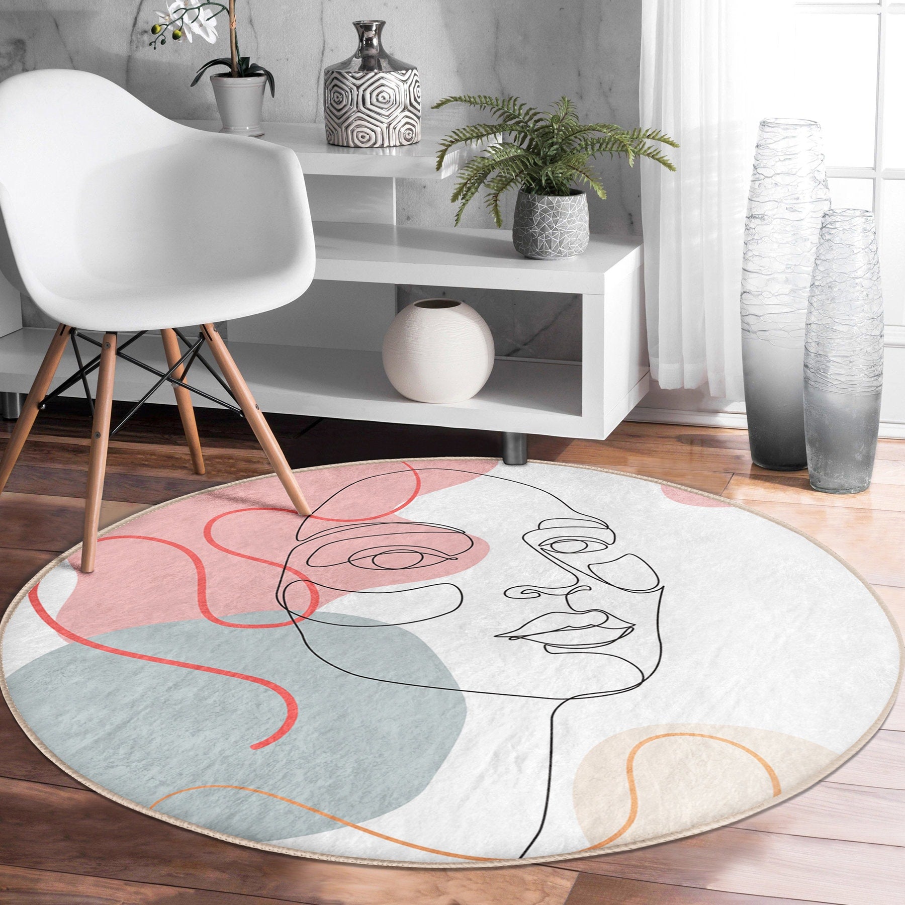 Modern living room with white chair, minimalist white shelf, potted plants, and round artistic rug featuring abstract face design