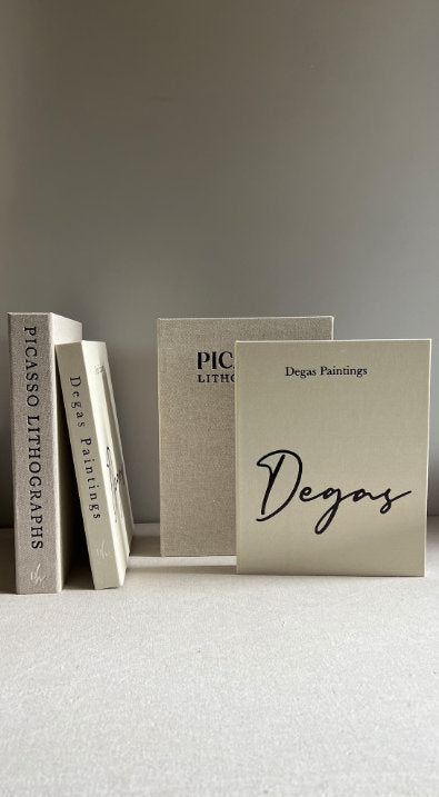 Three art books titled Picasso Lithographs and Degas Paintings displayed on a neutral surface with minimalistic background