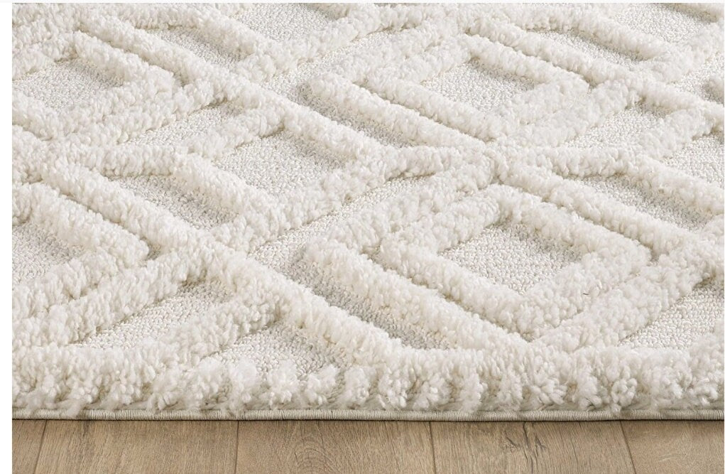 Close-up of a soft white textured area rug with raised diamond pattern on wooden floor