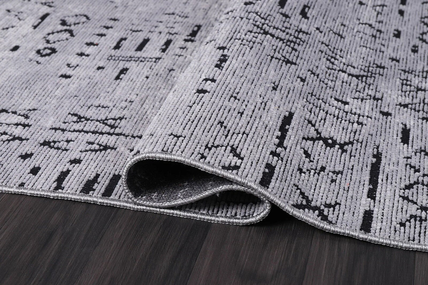 Close-up of folded gray patterned area rug on dark hardwood floor