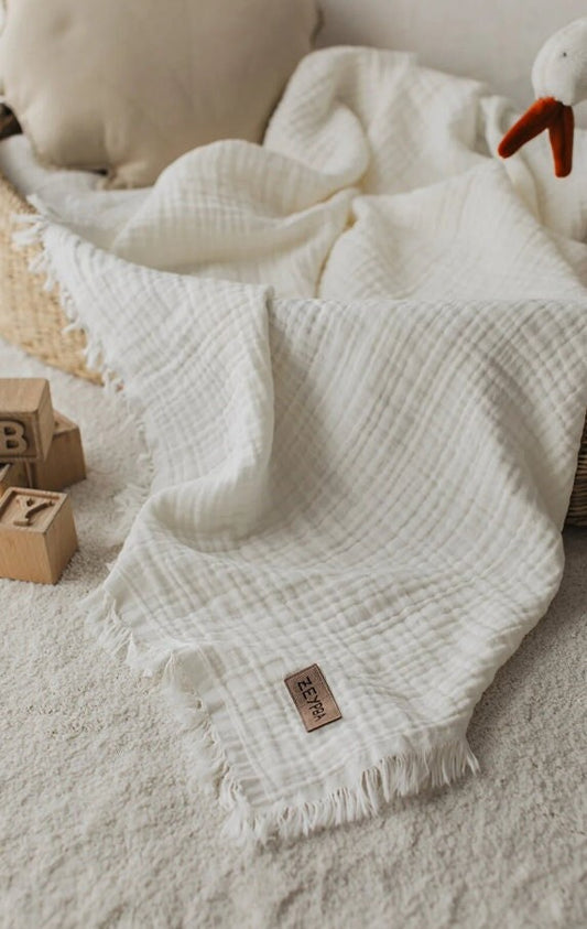 Soft white baby blanket with fringed edges in wicker basket on plush carpet with wooden alphabet blocks