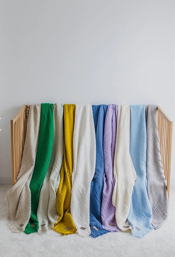 Colorful textured cotton blankets in green, yellow, white, blue, purple, and beige draped over wooden crib rails