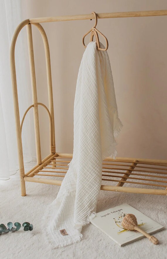 White textured blanket hanging on wooden rack with baby book and rattle on carpeted floor