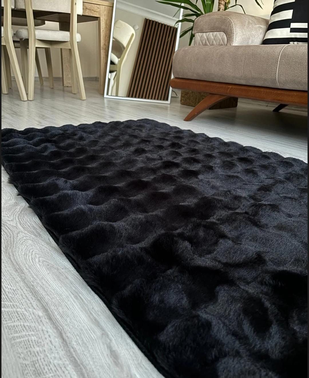 Black textured furry rug on light wood floor in modern living room with beige sofa and mirror