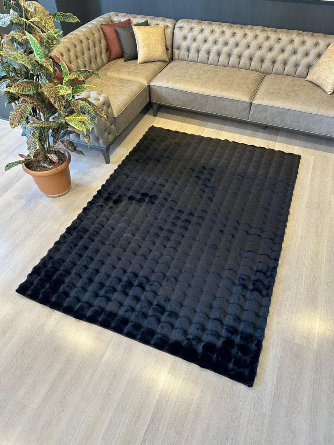 Modern living room with gray tufted sectional sofa, textured black rug, light wood floor, and potted plant