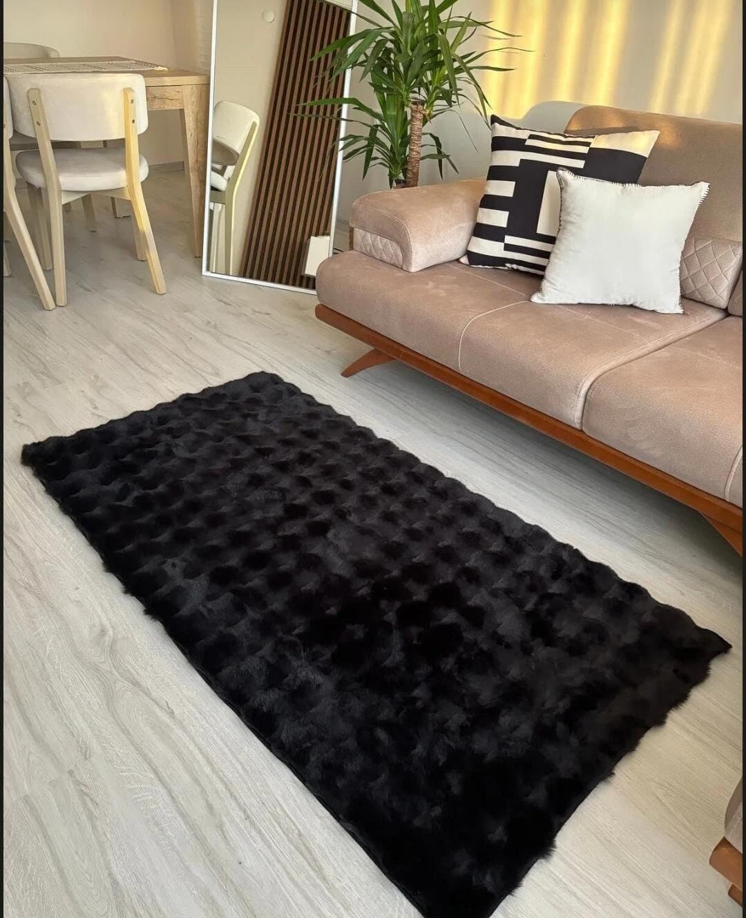 Modern living room with beige sofa, black and white pillows, black textured rug, light wood floor, and green plant